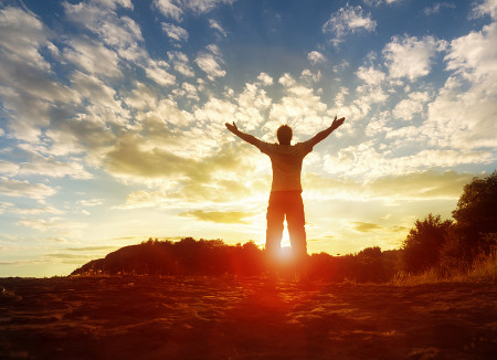 Silhouette of a man with hands raised in the sunset concept for religion, worship, prayer and praise